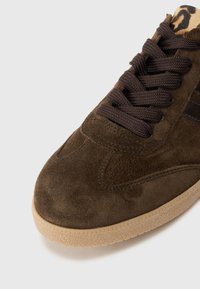 Sneaker en suède marron avec une tige texturée, des lacets brun foncé et une semelle en caoutchouc. Présente un détail en imprimé léopard au niveau du col.