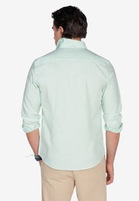 Camisa de manga larga verde menta claro con mangas arremangadas, textura suave, cuello tipo polo y corte recto en el dobladillo.