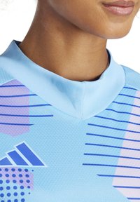 Lichtblauwe sporttop met een hoge kraag, voorzien van paarse en blauwe geometrische patronen en strepen, gemaakt van een gestructureerde, ademende stof.
