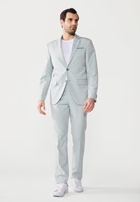 Costum gri deschis, cu un sacou cu un singur rând de nasturi, rever cu notch și două buzunare frontale. Asortat cu un tricou alb și teniși albi.