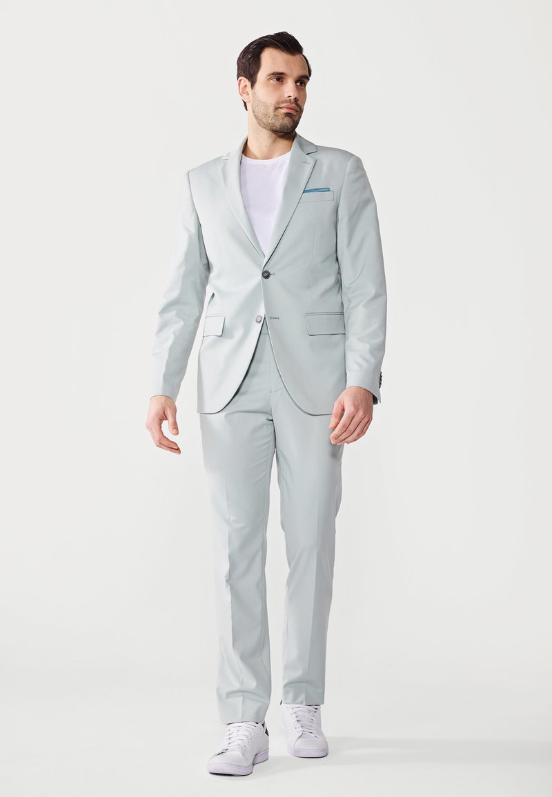 Costum gri deschis, cu un sacou cu un singur rând de nasturi, rever cu notch și două buzunare frontale. Asortat cu un tricou alb și teniși albi.