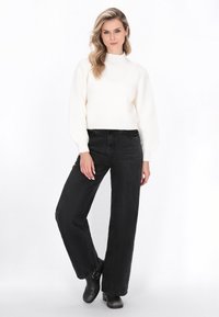 Hvid ribbet striktrøje med høj hals, parret med sorte vide jeans og sorte ankelstøvler. Glat struktur hele vejen igennem.