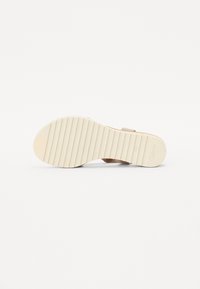 Sandale beige avec une semelle intérieure texturée et une large bride. La semelle en caoutchouc flexible présente des rainures horizontales pour la traction et l'adhérence.