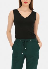 Czarny top bez rękawów z dekoltem w kształcie litery V, zestawiony z zielonymi spodniami z troczkiem i metalowymi dodatkami w pasie.