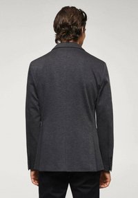 Blazer grigio scuro con una vestibilità su misura, rever a scelte e due spacco posteriori; presenta una trama liscia e polsini con bottoni.