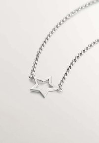 Collar de plata con un colgante en forma de estrella que presenta un centro abierto y una cadena texturizada. Los eslabones de la cadena son entrelazados y brillantes.