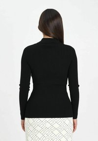 Top a maniche lunghe in maglia a coste nera con silhouette aderente e scollo con colletto, abbinato a una gonna a matita bianca con motivo fantasia.