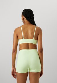 Ensemble de soutien-gorge et de shorts vert clair sans couture, avec des bretelles ajustables et une texture lisse et douce, vu de dos. Aucun motif ni élément matériel visible.