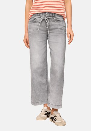 Kvinde iført falmede grå vidde jeans med bindebælte og beige sneakers med sorte striber, kombineret med en rødstripet top.