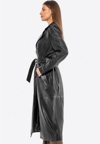 Abrigo de cuero negro con cintura ceñida, mangas largas, bolsillos laterales y textura suave; diseño hasta la rodilla con un corte ajustado.