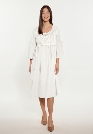 Valkoinen mekko, jossa on V-muotoiset pääntie ja kukka-ompelut bodice-osiolla. Siinä on kolme neljännesosa-mittaiset kello-hihat ja rento, virtaava siluetti.