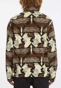 Veste en polaire brun et crème à motif, dotée d'un col haut, avec des formes abstraites et des lignes ondulées dans le dos. Texture douce.