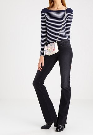 Femme portant un haut à manches longues rayé bleu marine et blanc, un jean bootcut noir, des bottes à talons noires et un petit sac bandoulière à motif floral.