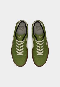Πράσινα αθλητικά παπούτσια με επάνω μέρος από σουέτ και ύφασμα, κρέμ κορδόνια και λαστιχένια σόλα. Διαθέτουν λογότυπο στη γλώσσα και διακοσμητικά στοιχεία στο πλάι.