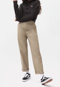 Sweat à capuche noir raccourci, pantalon beige à jambes droites et baskets noires avec accents blancs ; texture lisse et couleurs neutres.