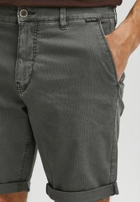Shorts en coton gris à coupe droite, avec fermeture à bouton, poches latérales et ourlets repliés. Texture lisse et détails de couture minimaux.