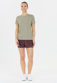 Camisa de manga corta verde oliva combinada con pantalones cortos deportivos burdeos y zapatillas blancas, con un diseño simple y un ajuste relajado.