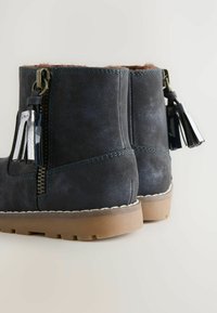 Bocanci până la gleznă din suede albastru închis, cu interior căptușit, fermoar lateral și ciucuraș decorativ; au o talpă din cauciuc maro cu prindere texturată.