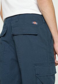 Marinblå cargoshorts gjorda av strukturerad tyg, med två bakfickor med klaffförslutningar och en Dickies-logga på midjebandet.