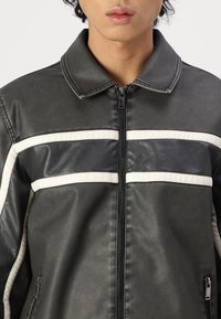 Black faux leather jacket with white horizontal stripes, collared design, zipper closure, and side pockets. Smooth texture, modern fit.