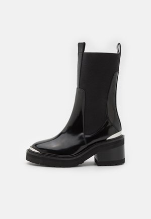Bota negra de cuero hasta la mitad de la pantorrilla con paneles laterales elásticos, tacón de bloque grueso, lengüetas para tirar y detalles metálicos en la puntera y el talón.