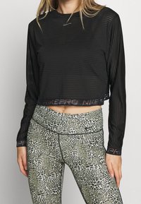 Maglietta nera a maniche lunghe con trama a righe orizzontali, caratterizzata da uno scollo rotondo e logo riflettente. Abbinata a leggings verde con stampa animale.