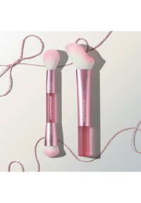 Twee Real Techniques make-upkwasten met roze handvat, witte en roze haren, geplaatst op een witte ondergrond met een roze-witte gedraaide draad.