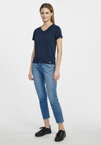 Granatowa koszulka z dekoltem w serek, krótki rękaw, miękki bawełniany materiał, w połączeniu z jasnoniebieskimi dżinsami i czarnymi sznurowanymi butami. Prosty, dopasowany krój.