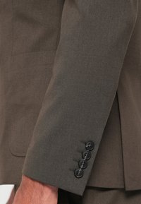 Brown tailored suit jacket sleeve with a smooth texture, featuring four black buttons and subtle stitching detail along the cuff.