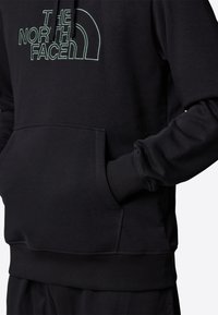 Black hoodie featuring a large green embroidered logo on the chest, a kangaroo pocket, ribbed cuffs, and a warm, soft texture.