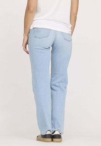 Jeans droits bleu clair avec une texture lisse, un discret détail sur les poches arrière, associés à des baskets noir et blanc.