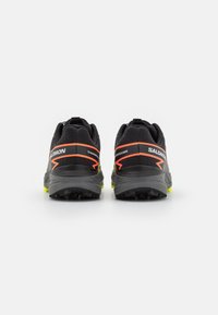 Scarpe da trail running nere con una parte superiore texturizzata, dettagli arancioni vivaci e suole gialle brillanti. Presentano un motivo di battistrada robusto per una buona aderenza.