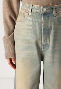 Lyseblå høytlivsjeans med en falmet, marmorert tekstur. Har detaljer med kobberknapp og sømmer, sidelommer og en avslappet passform.