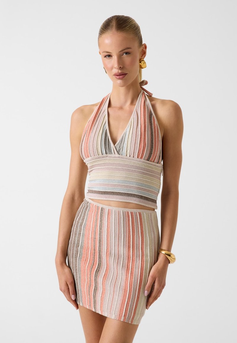 Femme portant un haut dos-nu sans manches et une mini-jupe rayée assortie dans des couleurs pastel douces, accessoirisée de boucles d'oreilles et d'un bracelet dorés.