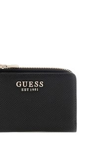 Portafoglio nero testurizzato con chiusura a zip, hardware dorato e marchio "GUESS EST 1981" sul davanti. Design rettangolare compatto.