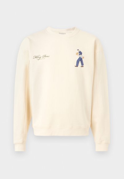 Cremfarbener Sweatshirt mit kleinem Motiv einer Person, die Baguettes trägt, und dem Text "Filling Pieces Baking Bread" auf der Brust.