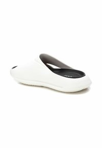 Zapato blanco de tipo slip-on con un exterior liso, punta redondeada y suave forro interior. La suela tiene un diseño de relieve sutil para mayor agarre.