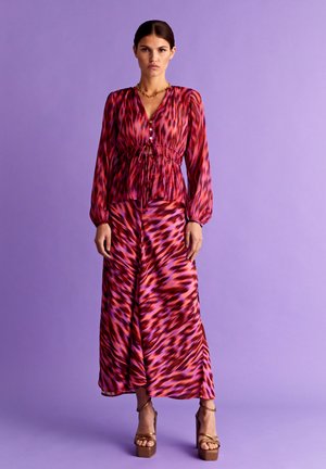 Maxi-Kleid in pinkem und lila abstraktem Muster, mit langen Ärmeln, gerafftem Bund und Knopfdetails. Kombiniert mit Plattform-Heels.