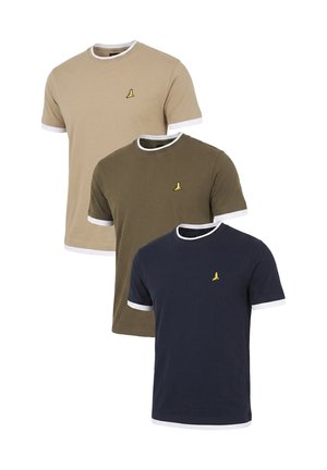 Giovane uomo con capelli corti e ricci che indossa una maglietta blu navy con bordo bianco, jeans blu e scarpe da ginnastica nere, in piedi davanti a uno sfondo semplice.