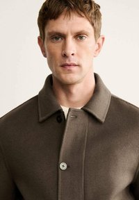 Cappotto in misto lana marrone con colletto, chiusura a un bottone e una texture morbida, mostrato su uno sfondo neutro.