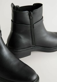Musthave mustad mustad, millel on külgzipper, tekstuuriga detailid ja kontrastsed õmblused tallal. Sile viimistlus ja ümar varvas.