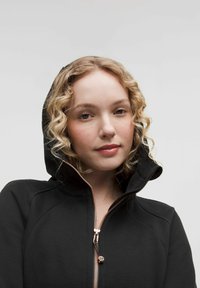 Black zip-up hoodie with a high collar, featuring a rose gold zipper and drawstring. Soft texture with subtle seam details.