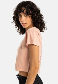 Lys rosa cropped t-skjorte i myk bomull. Korte ermer med grafisk trykk foran og på siden. Enkel design med en avslappet passform.