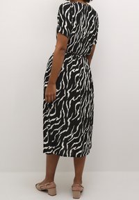 Robe à imprimé zèbre noir et blanc, manches courtes, taille cintrée, ourlet à hauteur du genou, associée à des sandales à talons beiges.