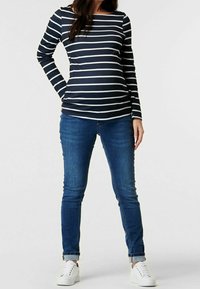 Marinrandig långärmad topp med rund halsringning, i kombination med blå smala jeans och vita sneakers, vilket visar en avslappnad outfit.