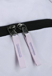 Un sac à dos blanc en matériau texturé ; il est doté d'une fermeture éclair noire et de deux tirettes métalliques YKK avec des boucles lilas.