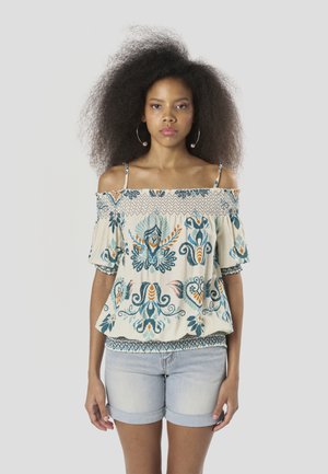 Blusa estilo off-shoulder en color crema con bordado floral en azul, naranja y verde. Mangas cortas con vuelo y dobladillo inferior elástico. Combinada con shorts de mezclilla clara.