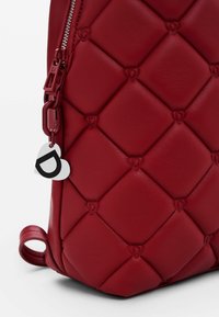 Bolso de mano de cuero rojo con patrón acolchado, que presenta un motivo de corazón y herrajes plateados. Incluye un charm con un corazón y la letra "D."