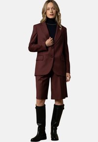 Set composto da blazer bordeaux e pantaloni corti in un tessuto liscio, con chiusura a un bottone, pantaloni corti fino al ginocchio e stivali neri alti fino al ginocchio.