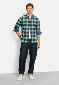 Karierte grüne und marineblaue Hemd mit hochgekrempelten blauen Jeansärmel, kombiniert mit dunklen Jeans und weißen Turnschuhen. Schlichtes, lässiges Design.